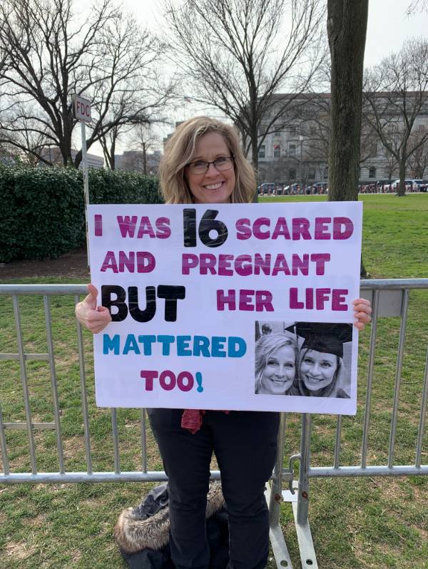 Marcher holds up a sign with image of her and her graduate daughter, with the words, 